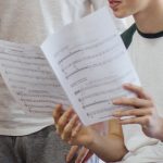 Male teenagers are in a music lesson at school. They are discussing sheet music with their teacher.