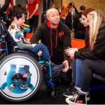 A young person in a wheelchair talks to a group of smiling adults