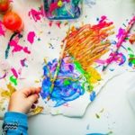 Birds eye view of a table that has brightly coloured paint and paintbrushes